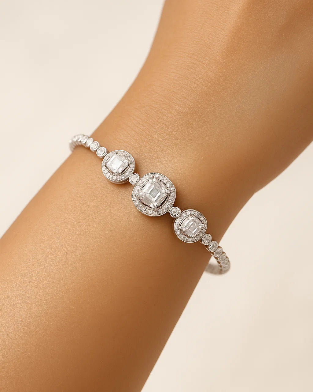 Silver bracelet with emerald-cut gemstones on a wrist against a beige background