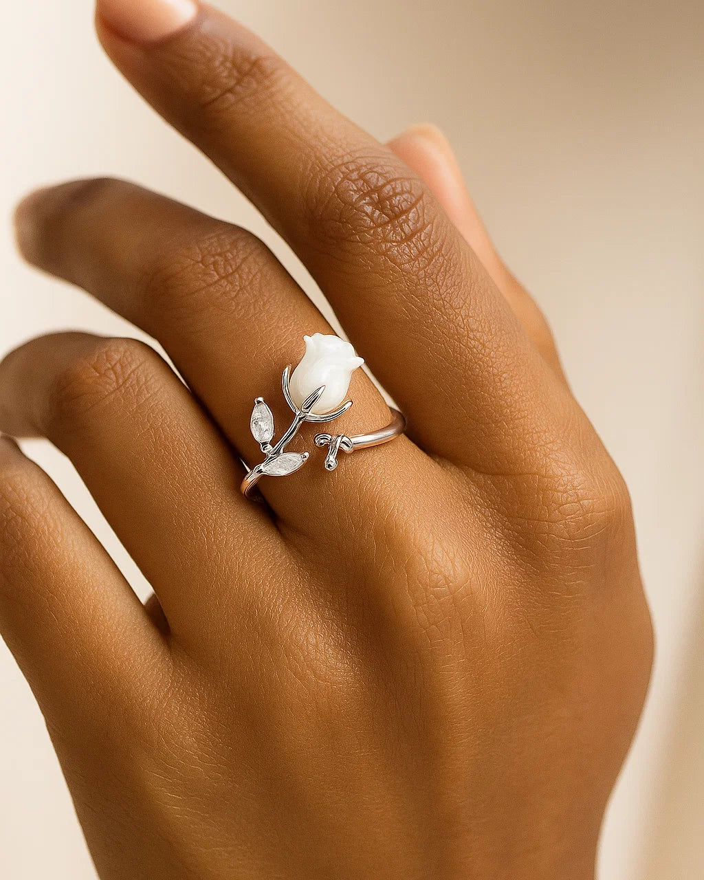 Silver ring with a white floral design on a hand against a beige background