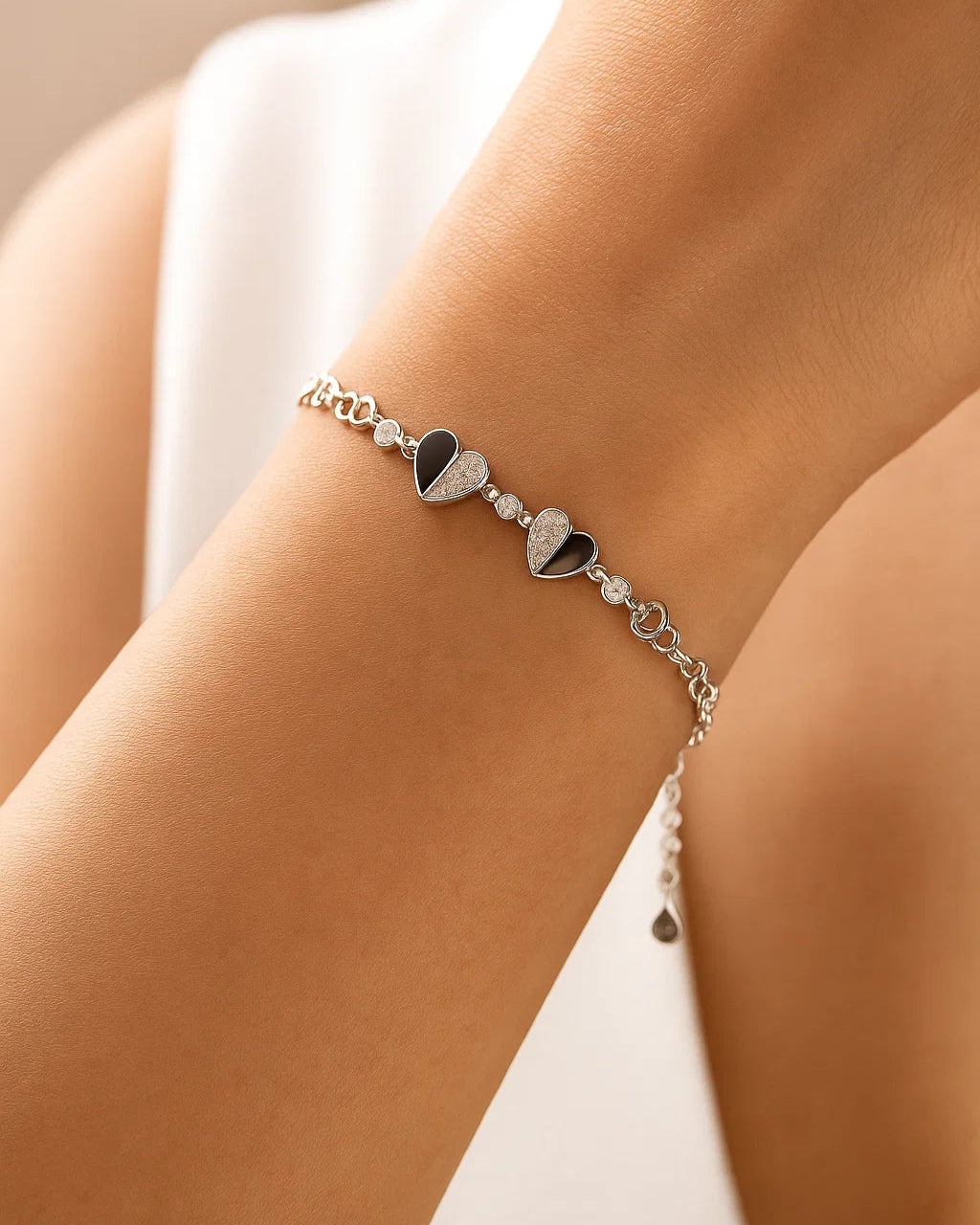 Silver bracelet with heart charms on a wrist against a neutral background
