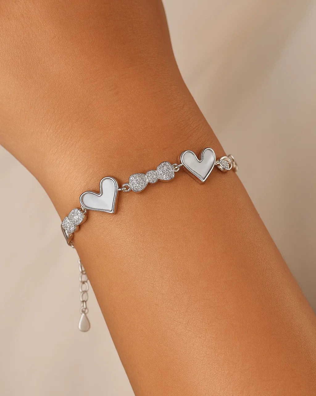 Silver bracelet with heart charms on a wrist against a beige background