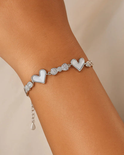 Silver bracelet with heart charms on a wrist against a beige background