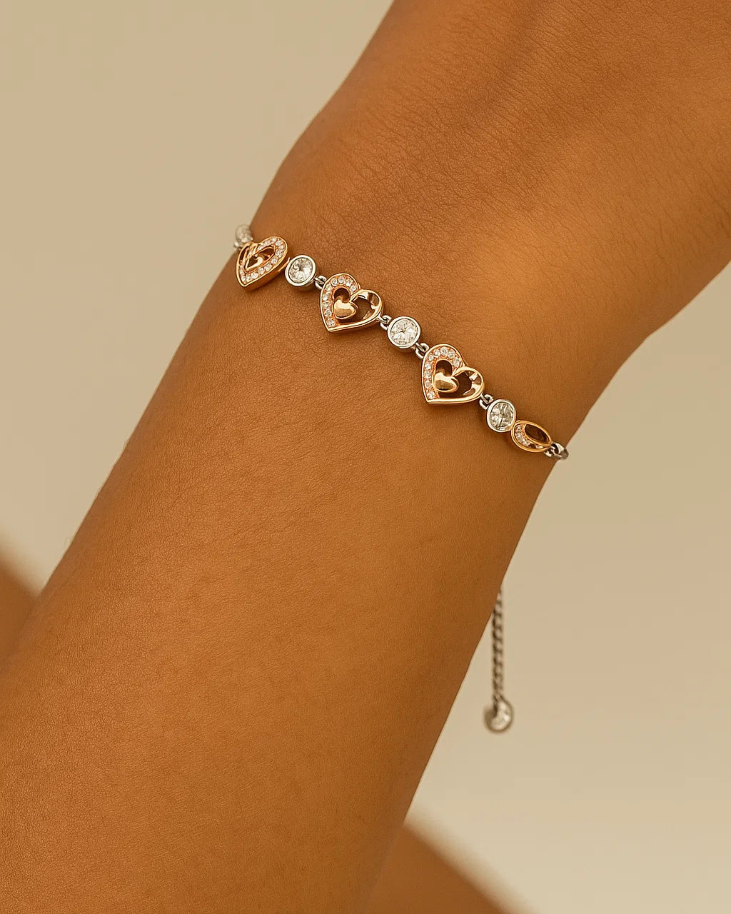 Rose gold bracelet with heart-shaped charms on a wrist against a beige background