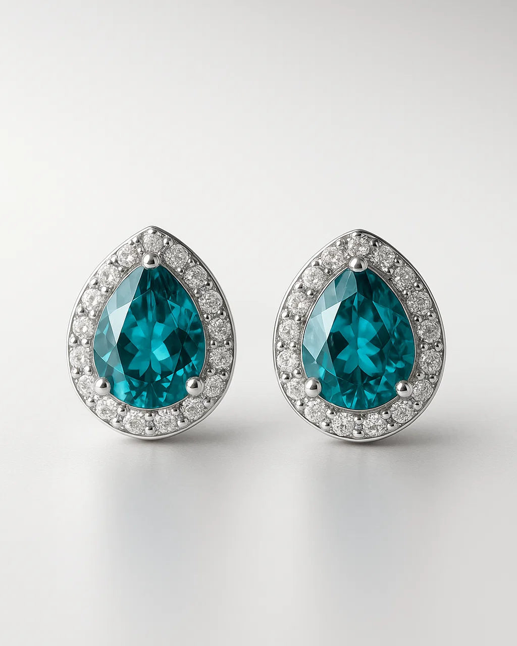 Pair of teal teardrop earrings with silver rims on a light gray background