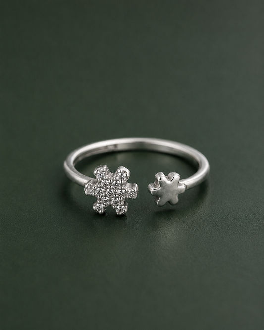 A silver open ring featuring two snowflake-shaped settings, one pavé-set with small clear stones and one plain, displayed on a dark green background.