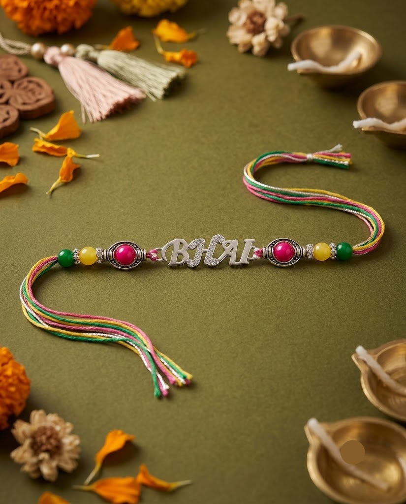 A personalized Rakhi featuring the name 'BHAI' in silver script, flanked by pink and yellow beads, resting on a dark olive green surface surrounded by festive props like marigold petals, brass oil lamps, and tassel garlands.