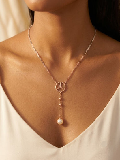 A close-up of a model wearing a delicate rose gold necklace with a Mercedes-Benz star pendant and a dangling pearl, styled with a white V-neck top.