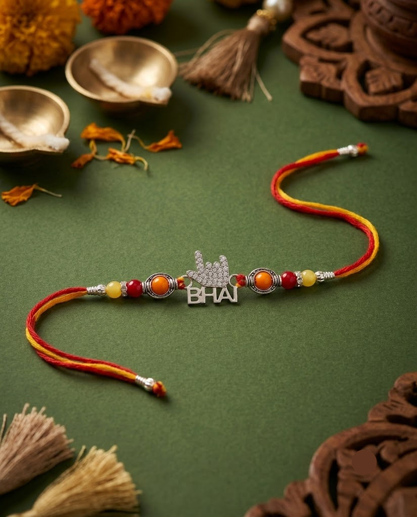 A traditional Indian Rakhi with a silver 'BHAI' nameplate and red, orange, and yellow beads, displayed on a dark green textured background with festive decorative props.