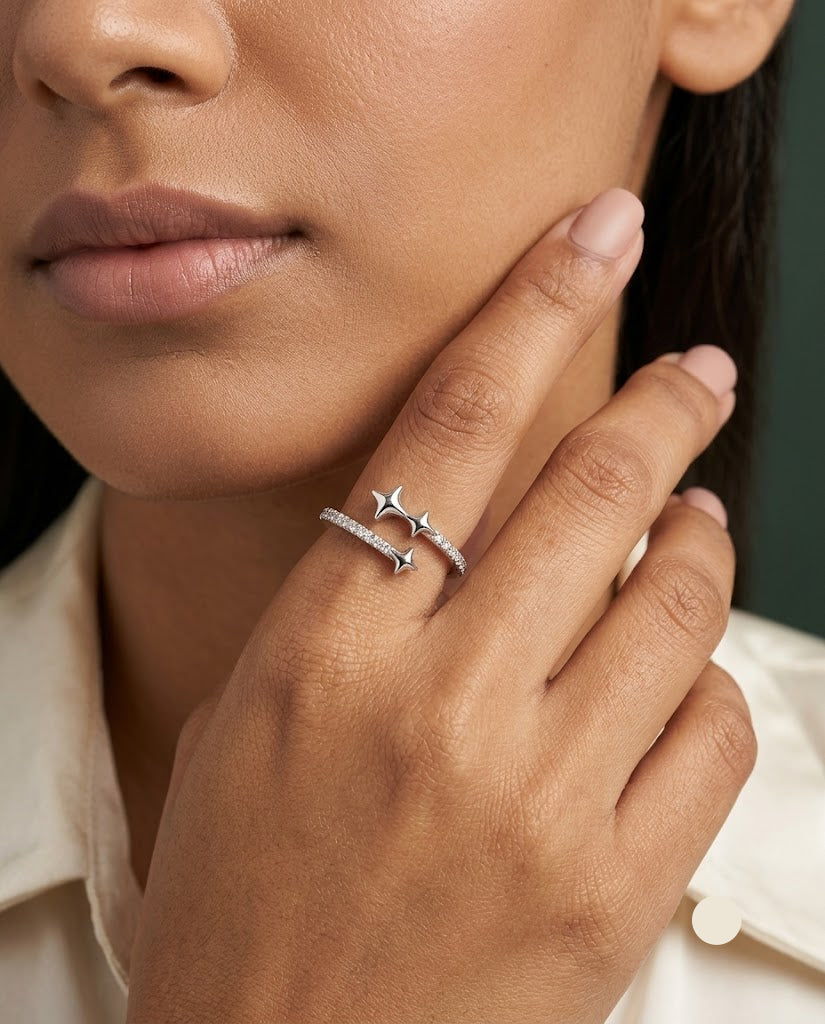 A close-up of a model's hand and lower face wearing a delicate silver ring with two small star motifs on a slim band.