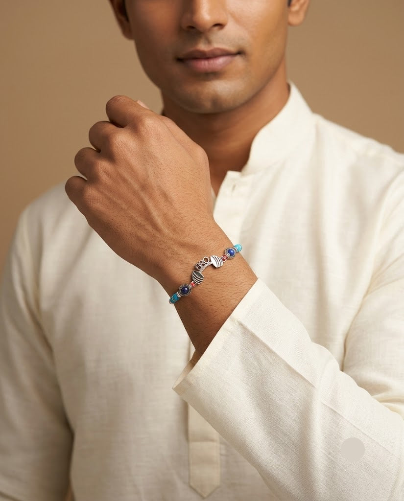 A man wearing a white linen kurta and adjusting his collar, showcasing a silver-toned chain bracelet with blue and purple beads on his wrist, set against a warm beige background.