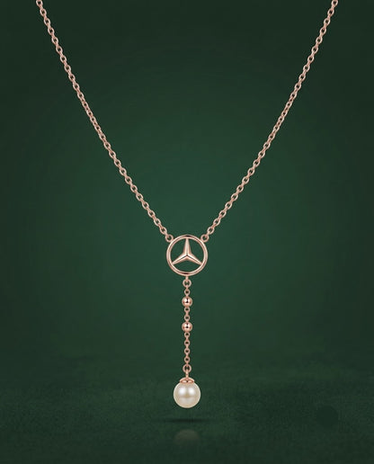 A rose gold necklace featuring a Mercedes-Benz three-pointed star logo pendant, with a dangling pearl bead at the bottom, set against a dark green background.