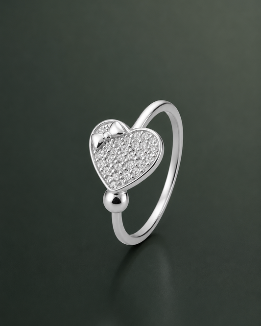 A silver heart-shaped ring with a pavé-set clear stone center and a polished ball accent, shown on a dark reflective background.